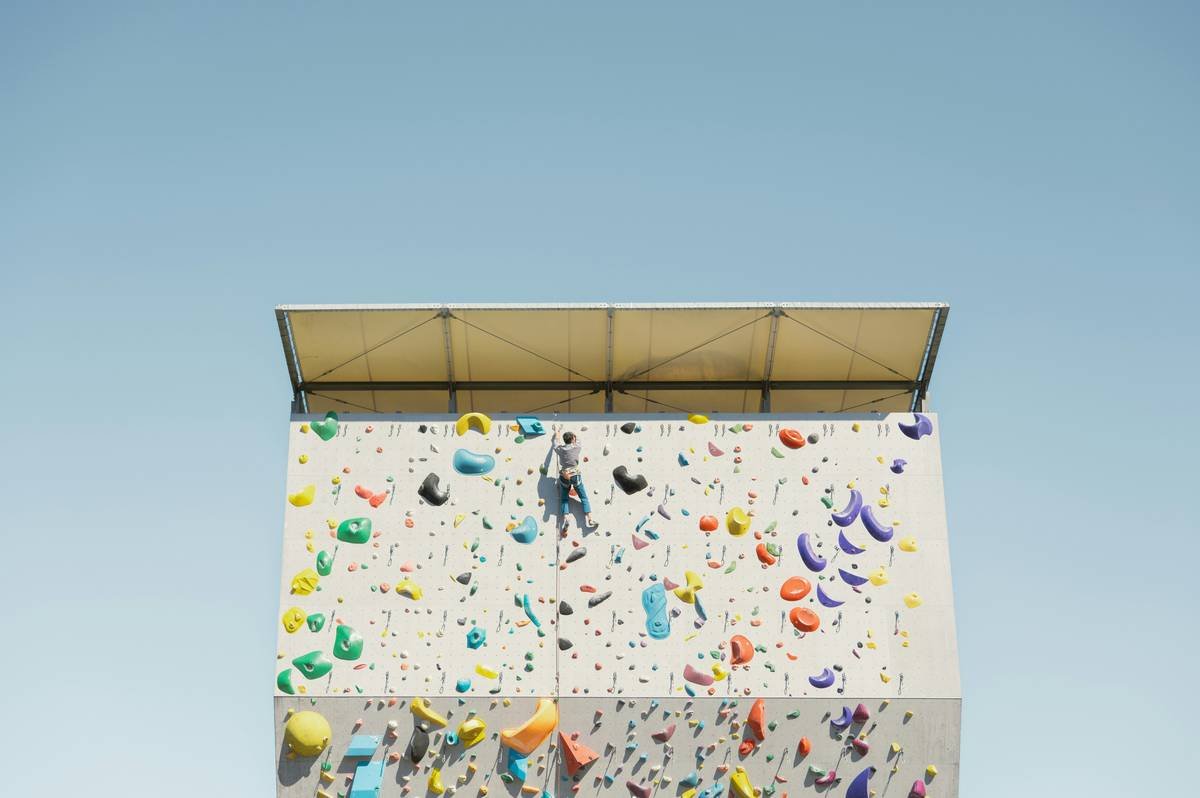 Infographic comparing essential vs. advanced beginner rock climbing gear: harness, shoes, helmet, rope, belay device vs. tricams, big wall haul bags, adjustable daisies